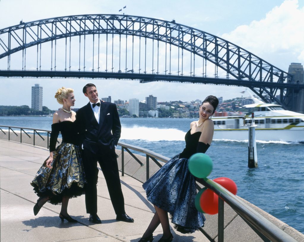 three models in evening wear with Sydney Opera House and Sydney Harbour Bridge in the background, fashion by Studibaker Hawke.
